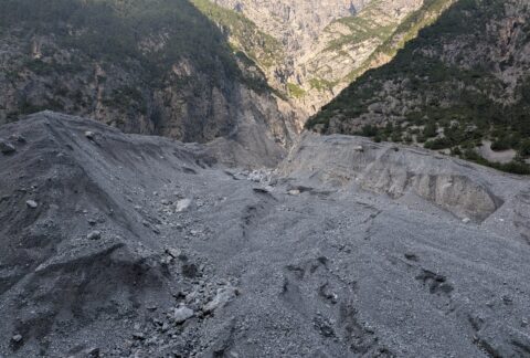 Rugged gray scree slope at the base of a steep rocky canyon with sparse trees along the sides