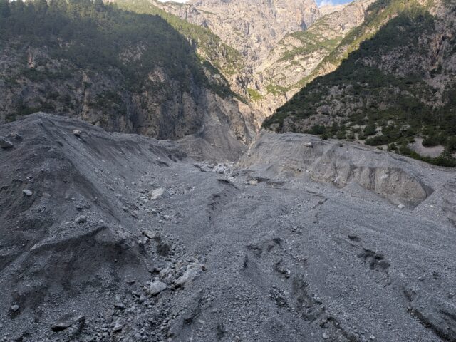 Rugged gray scree slope at the base of a steep rocky canyon with sparse trees along the sides
